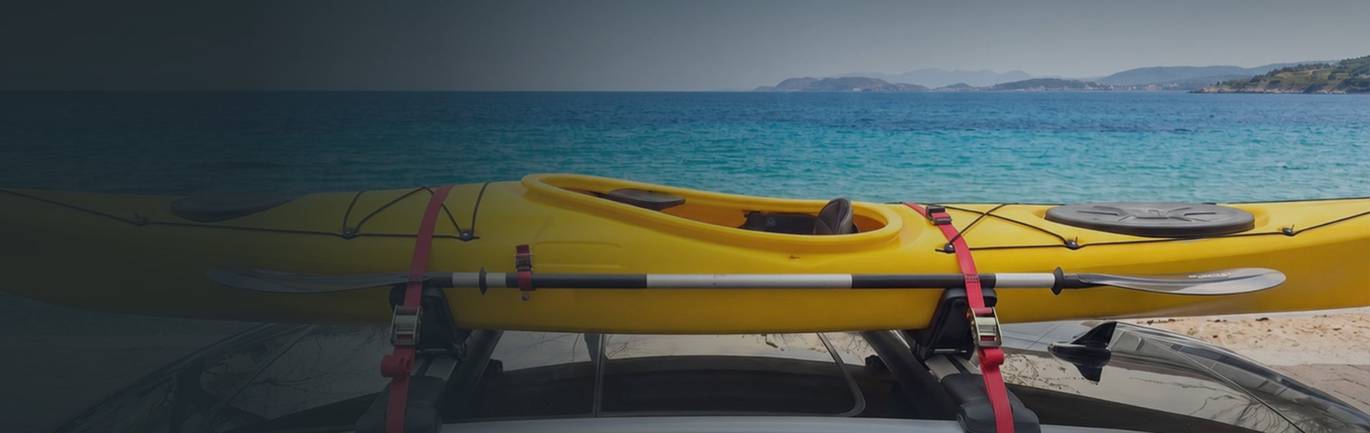 Yellow kayak on Axenture roof cross bars beside a summer sea, ready for a road trip
